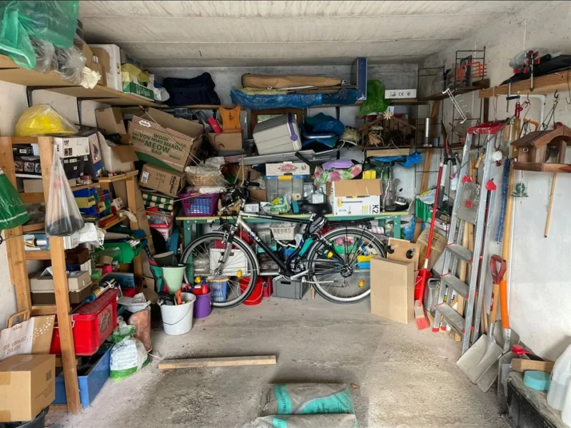Vollständig belegte Garage mit Regalen, Fahrrad, Werkzeug und Gartengeräten vor der Entrümpelung
