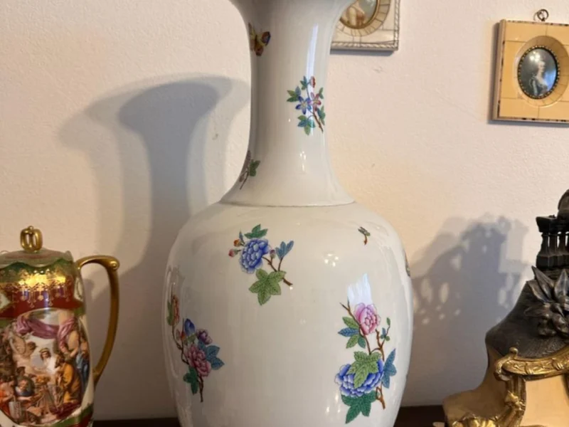 Große Porzellanvase mit Blütendekor vor einer Wand mit Miniaturen
