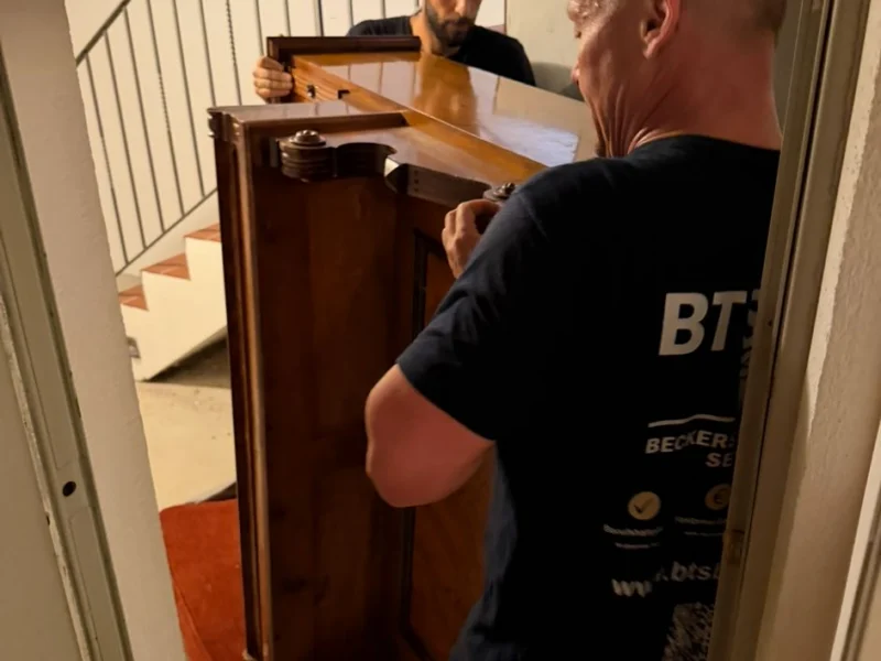 Zwei Mitarbeiter von BTS Bavaria tragen einen antiken Kleiderschrank durch ein Treppenhaus