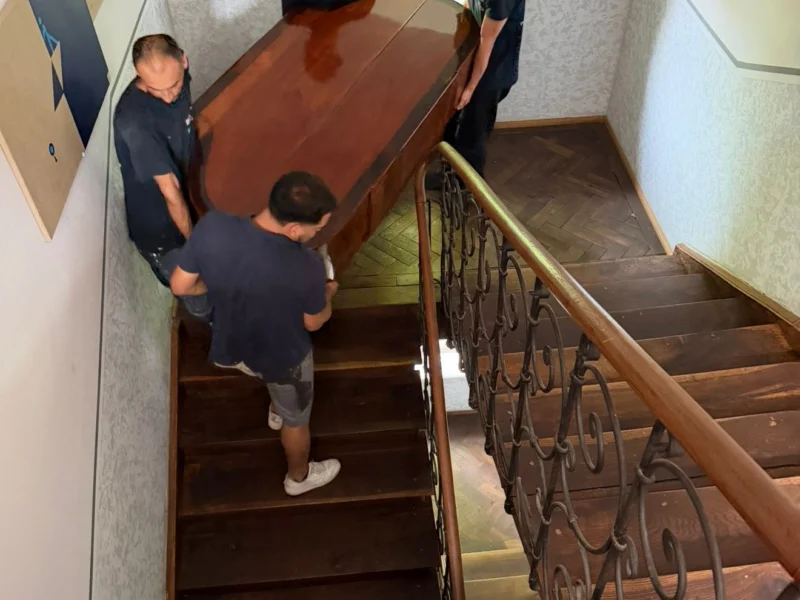 Vier Mitarbeiter von BTS Bavaria tragen gemeinsam ein Klavier durch ein Treppenhaus