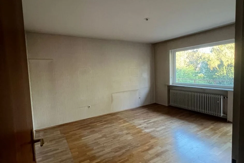 Vollständig geräumter Wohnraum mit Parkett und großem Fenster