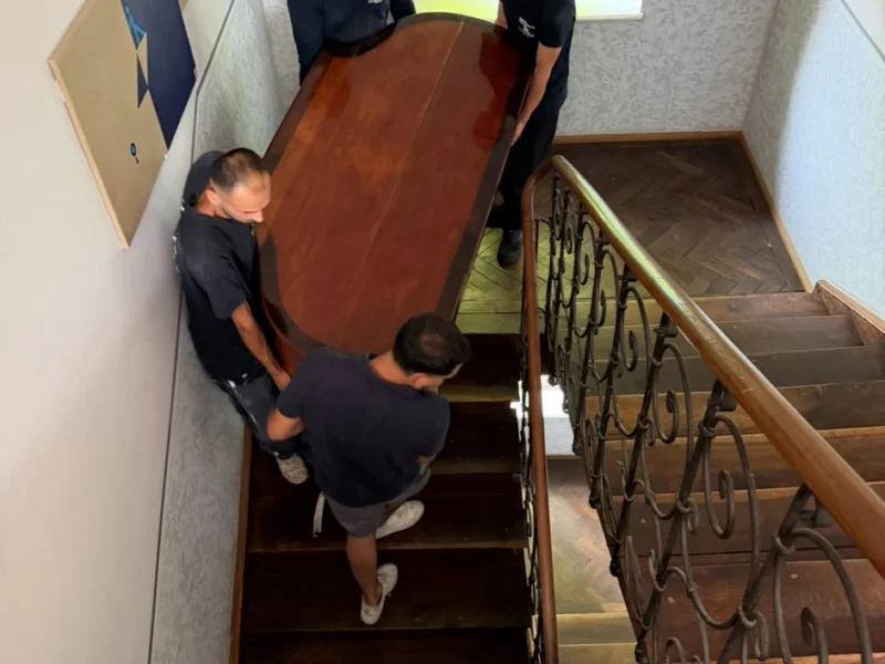 Mitarbeiter tragen gemeinsam ein großes Holzmöbel im Treppenhaus