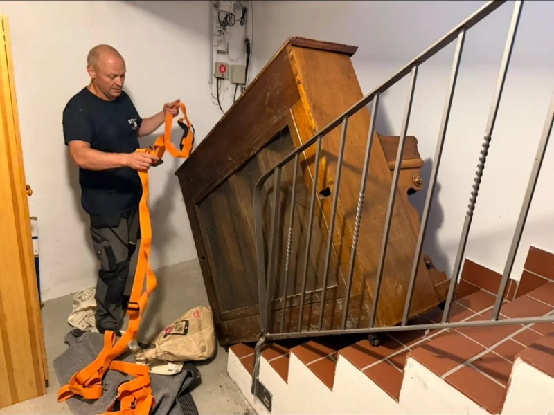 Mitarbeiter mit Tragegurt neben einem großen Holzmöbel im Treppenhaus